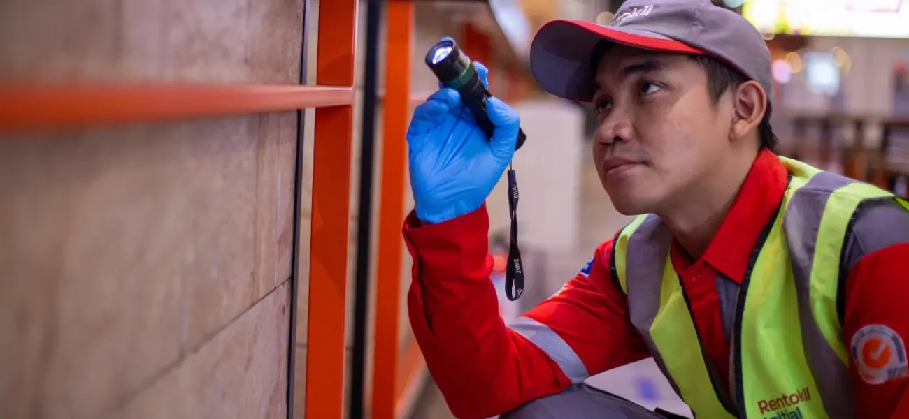 A Rentokil Pest Control technician shines a flashlight under a door in search of unwanted pests