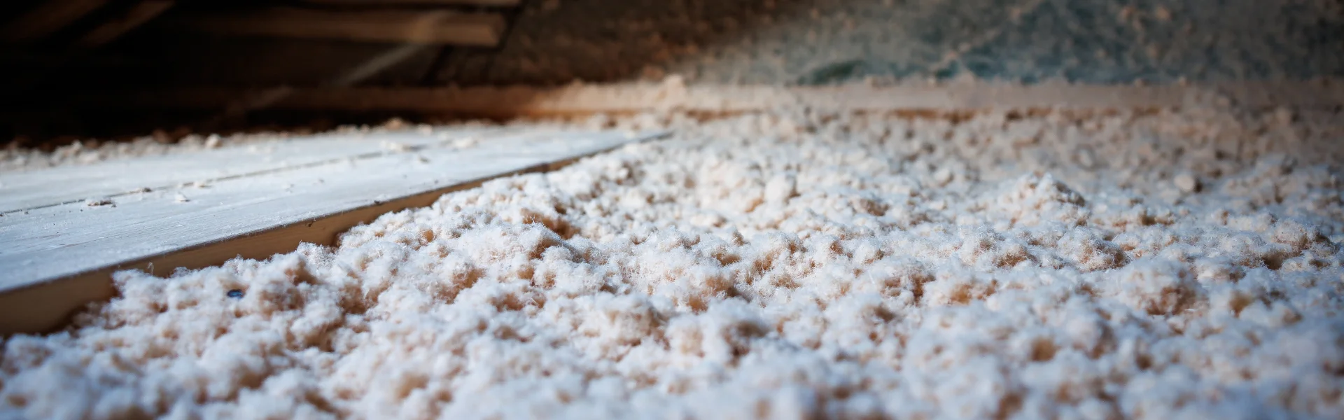 Low-angle wide shot focusing on the textured surface of fluffy, light-colored insulation filling a wooden attic space.
